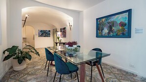 A dining area with a glass table, teal chairs, a potted plant, and a colorful abstract painting on the wall. - The Prince's "Casena" - Historic home with a sea view (Palermo)
