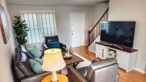 A living room with a sofa, armchairs, a coffee table, a TV, and a staircase. - The Cozy Corner, 2-bedroom townhome in charming Newark with WiFi, and parking (Newark)