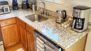 A kitchen with wooden cabinets, granite countertops, a dishwasher, a coffee maker, and a window with plants. - The Cozy Corner, 2-bedroom townhome in charming Newark with WiFi, and parking (Newark)