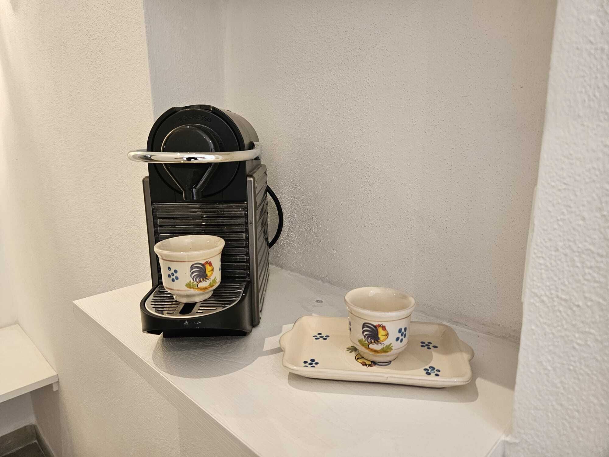 Une machine à expresso noire, avec deux tasses posées sur un plateau, toutes deux ornées de motifs représentant des coqs.