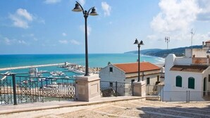 A coastal view with a marina, buildings with red-tiled roofs, and a clear sky.
