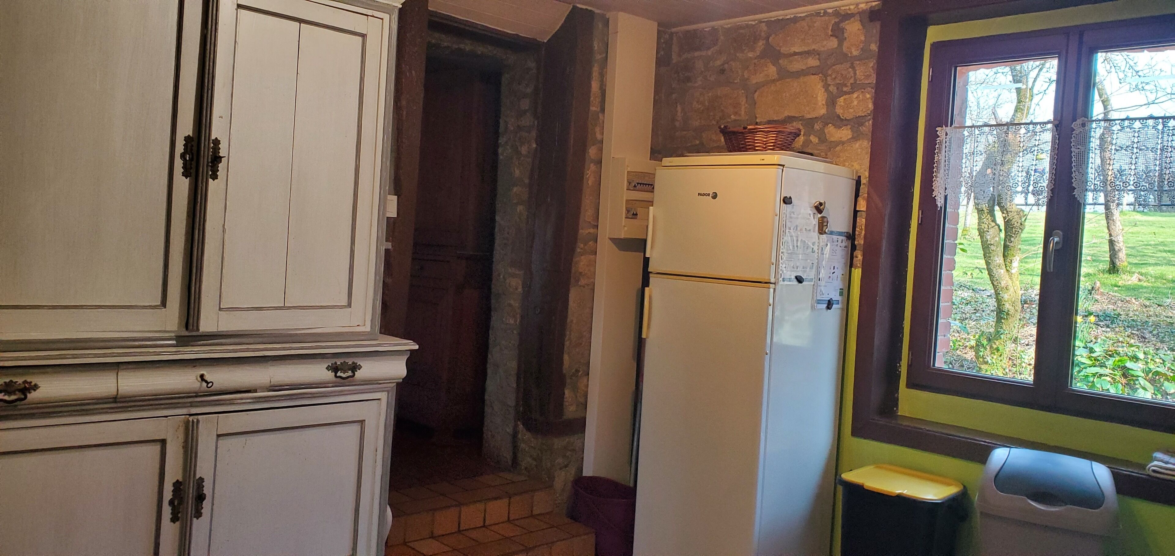 A kitchen with white cabinets, a white refrigerator, and a window with lace curtains.