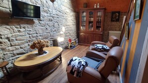 Une pièce chaleureuse avec un mur en pierre, un meuble en bois, des fauteuils en cuir et une table ronde.