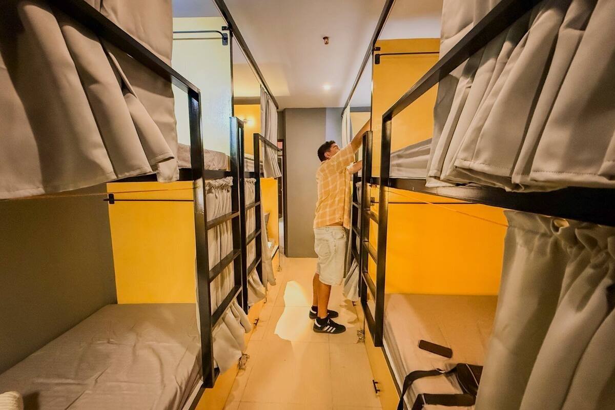 A narrow corridor with bunk beds, each with a mattress and a blanket.