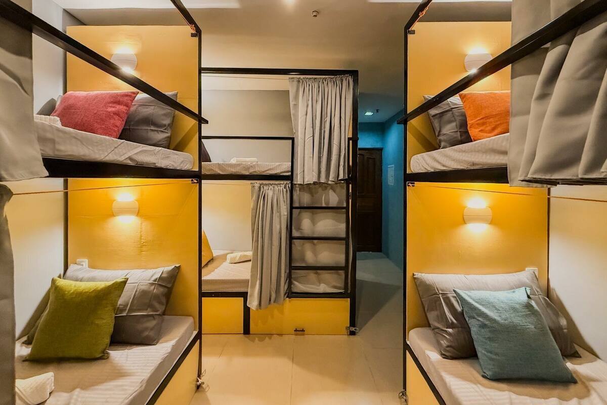 A dormitory room with bunk beds, a ladder, and a curtain.