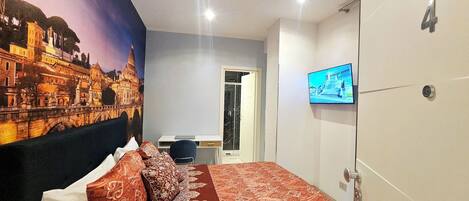 Ett hotellrum med en säng, ett skrivbord, en tv och en dörr.