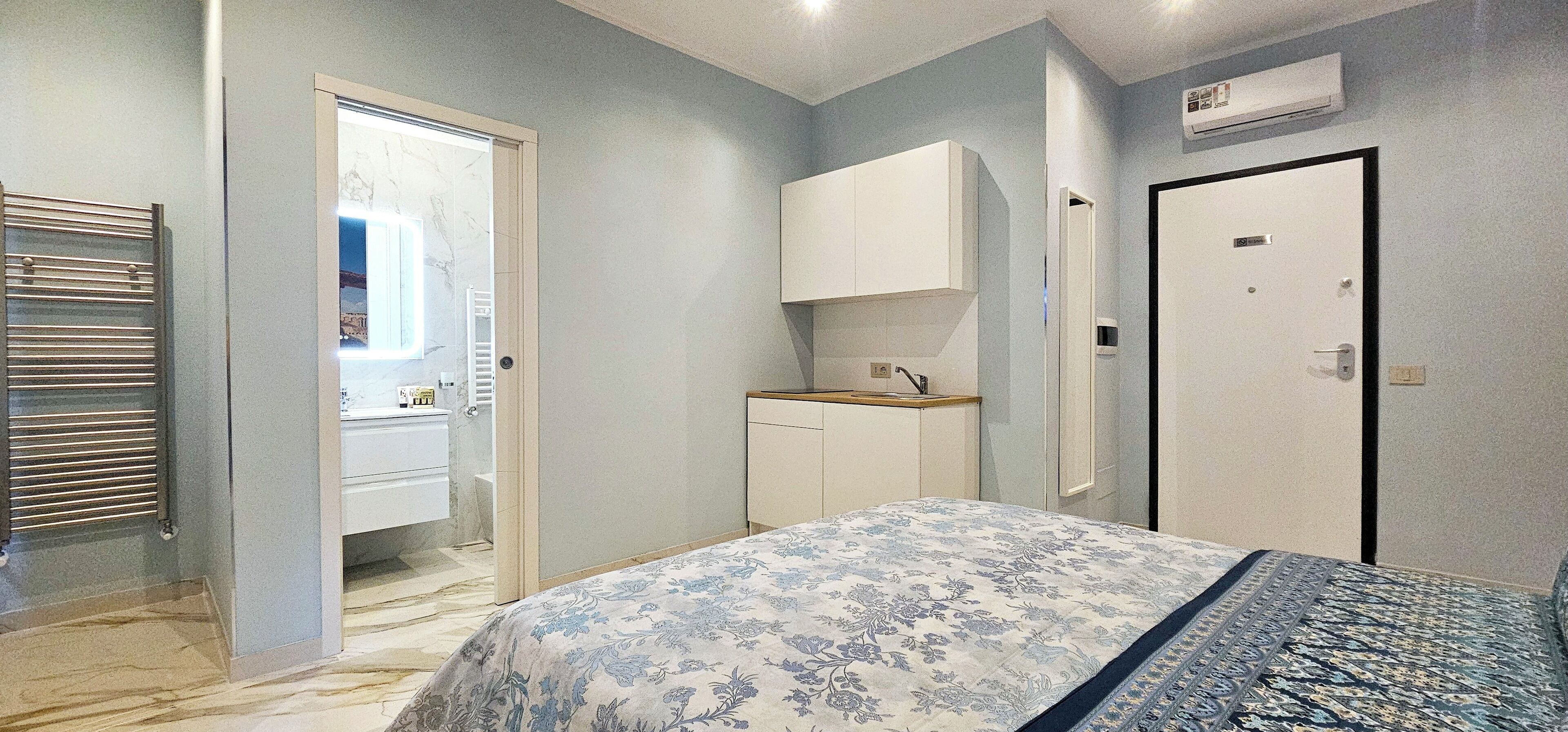 A bedroom with a bed, a wardrobe, a small cabinet, and a door.