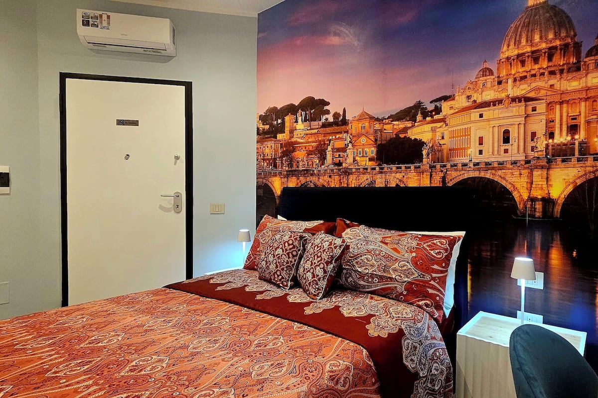 A hotel room with a large bed, a desk with a laptop, and a wall mural of a historic building.