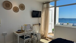 Una habitación con cama, un escritorio con sillas, un televisor y una ventana con vista al mar.