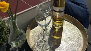 Una terraza con vistas a la playa, una botella de vino, dos copas y flores amarillas.