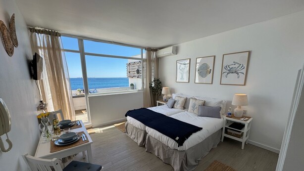Un dormitorio con una cama grande, un escritorio con una silla, una ventana con vista al mar y obras de arte en la pared.