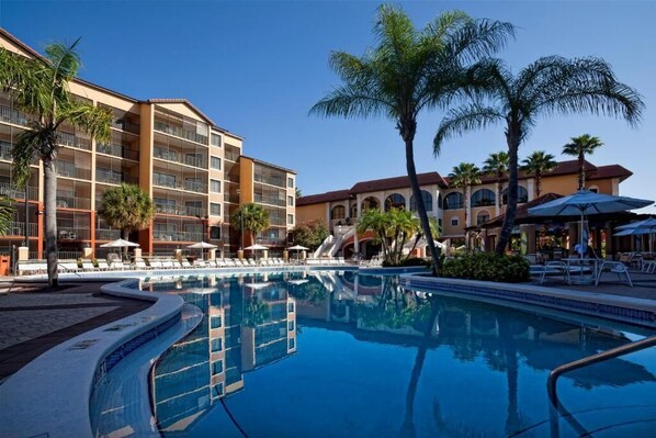 A hotel with a swimming pool surrounded by palm trees and lounge chairs.
