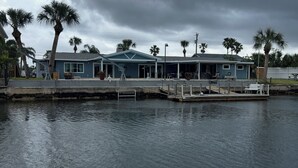 Ein Haus am Wasser mit einer Anlegestelle, Palmen und einem bewölkten Himmel.