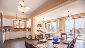 A spacious kitchen with modern appliances, a dining area with a large table set for six, and a view of a swimming pool. - Sunset Vista Exclusive villa (Zakynthos)