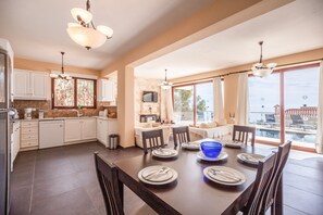 A spacious kitchen with modern appliances, a dining area with a large table set for six, and a view of a swimming pool.