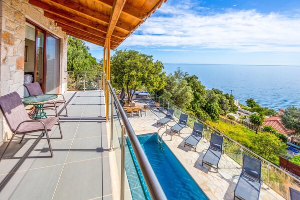 A balcony with a pool, lounge chairs, and a table.