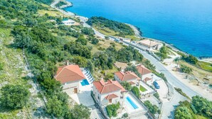 An aerial view of a coastal property with multiple buildings, a winding road, and a clear view of the sea. - Sunset Vista Exclusive villa (Zakynthos)