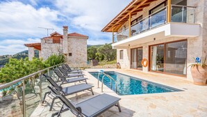 A poolside area with lounge chairs, a swimming pool, and a stone building with a balcony. - Sunset Vista Exclusive villa (Zakynthos)