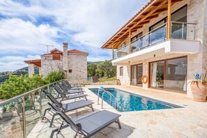 A poolside area with lounge chairs, a swimming pool, and a stone building with a balcony.