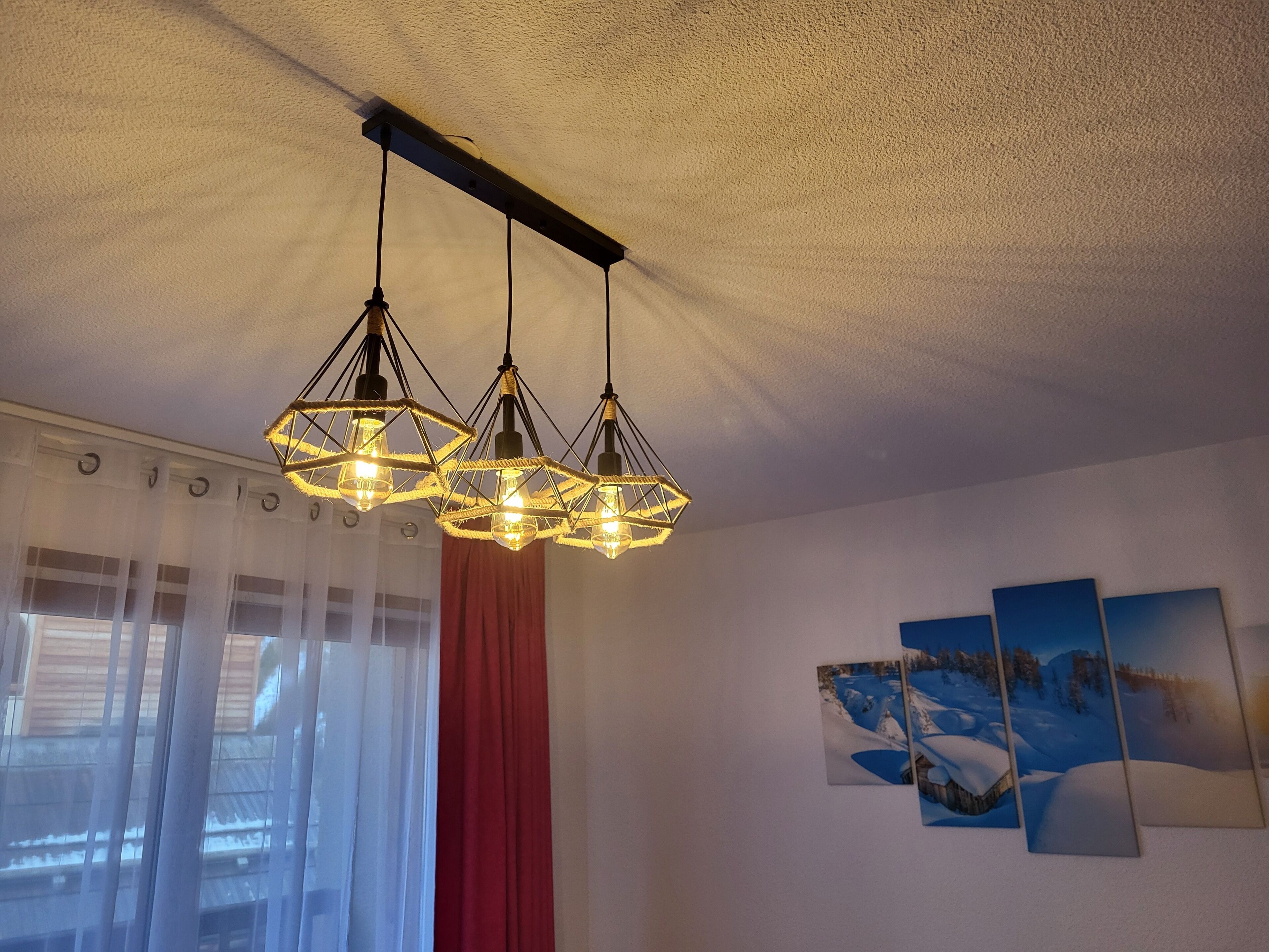 A room with a ceiling-mounted light fixture and a window with sheer curtains.