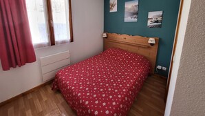 Un dormitorio con cabecera de madera, colcha estampada de flores rojas y tres cuadros en la pared.