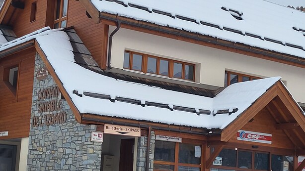 Un edificio con fachada de piedra, vigas de madera y techo cubierto de nieve.