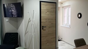 Een moderne woonkamer met een flatscreen televisie aan de muur, een houten deur, een raam en een eethoek met een tafel.