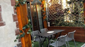 Een terras met een houten pergola, kunstgras en een tafel met stoelen.