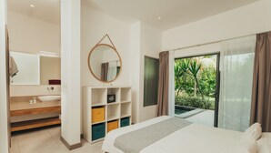 A modern bedroom with a large bed, a built-in vanity with a mirror, and a view of a lush garden through a sliding glass door. - Lakaz Filao - Premium Apt - private pool & garden (Grande Riviere Noire)
