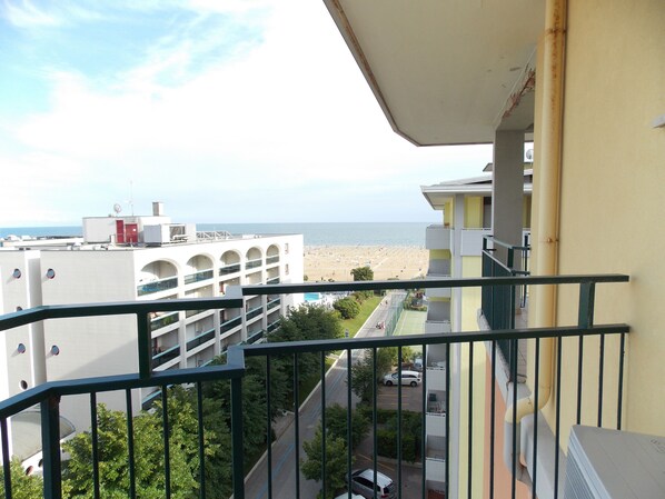 A balcony with a view of a beach and a parking lot.