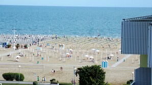 Una playa con numerosos sombrillas y tumbonas, un cielo despejado y el océano al fondo.