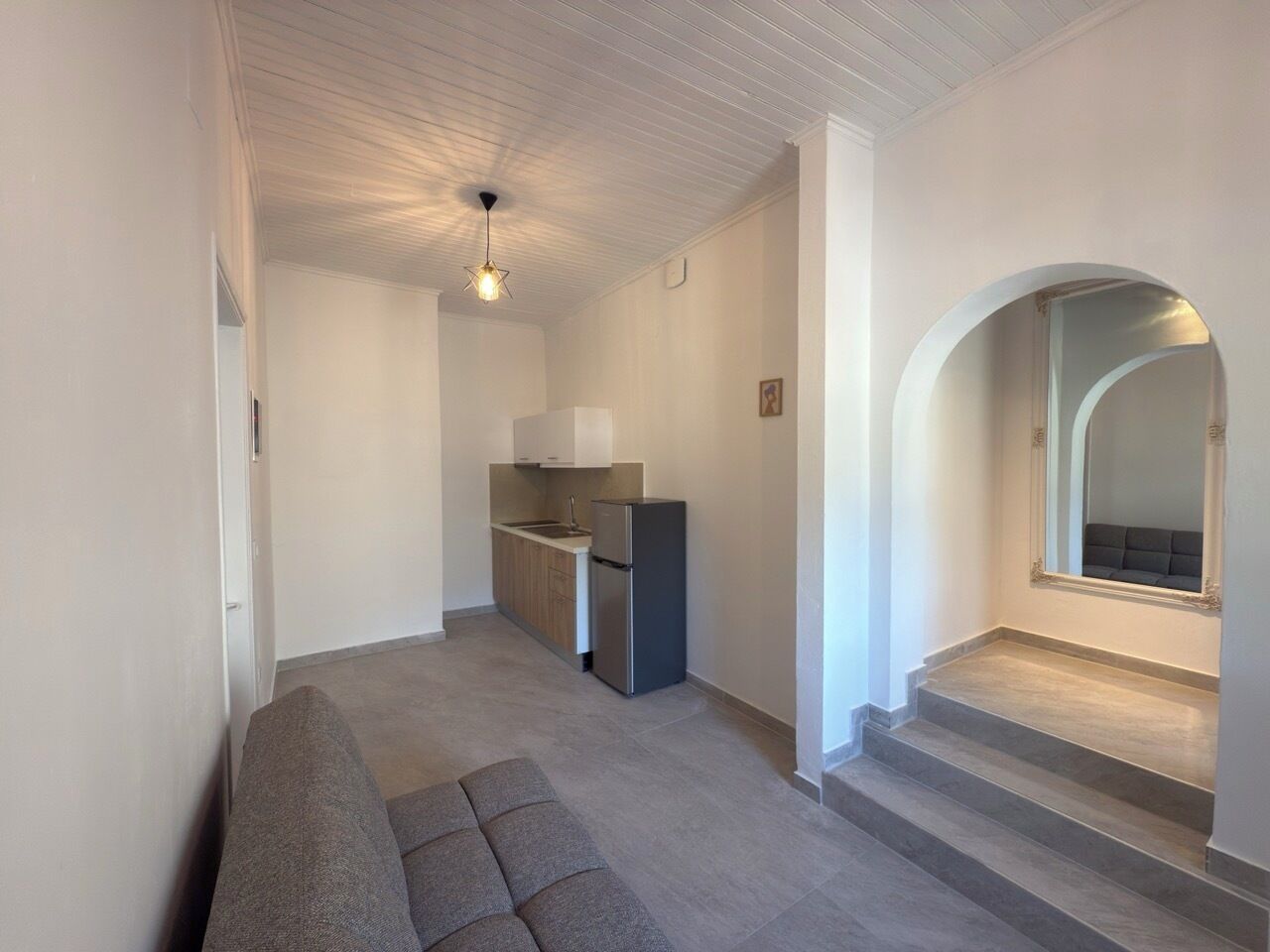 A modern apartment with a kitchenette, a sofa, and a staircase leading to an upper level.