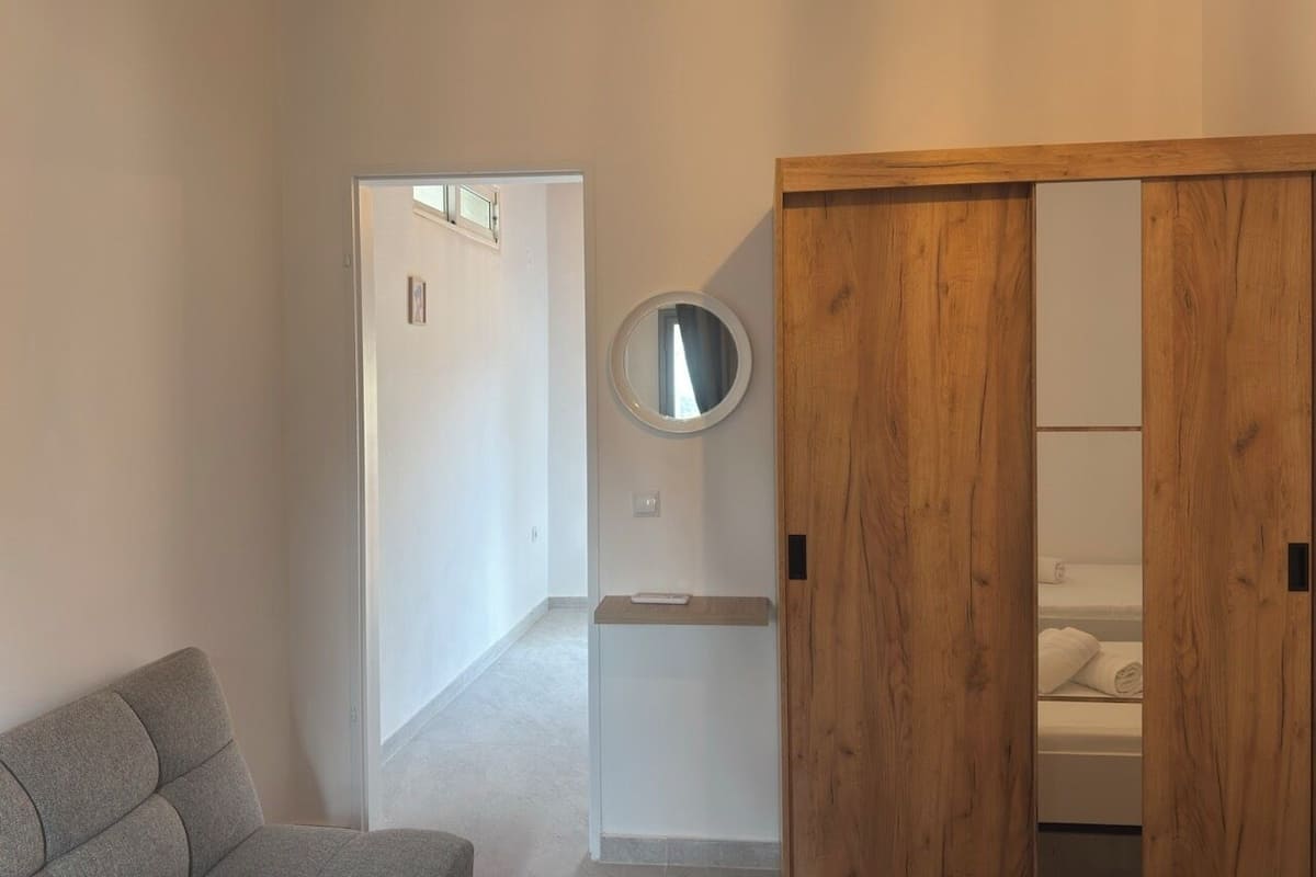 A bedroom with a wooden wardrobe, a round mirror, and a grey sofa.