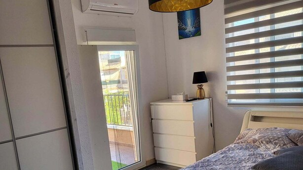 A bedroom with a bed, a dresser, a lamp, and a window with blinds.