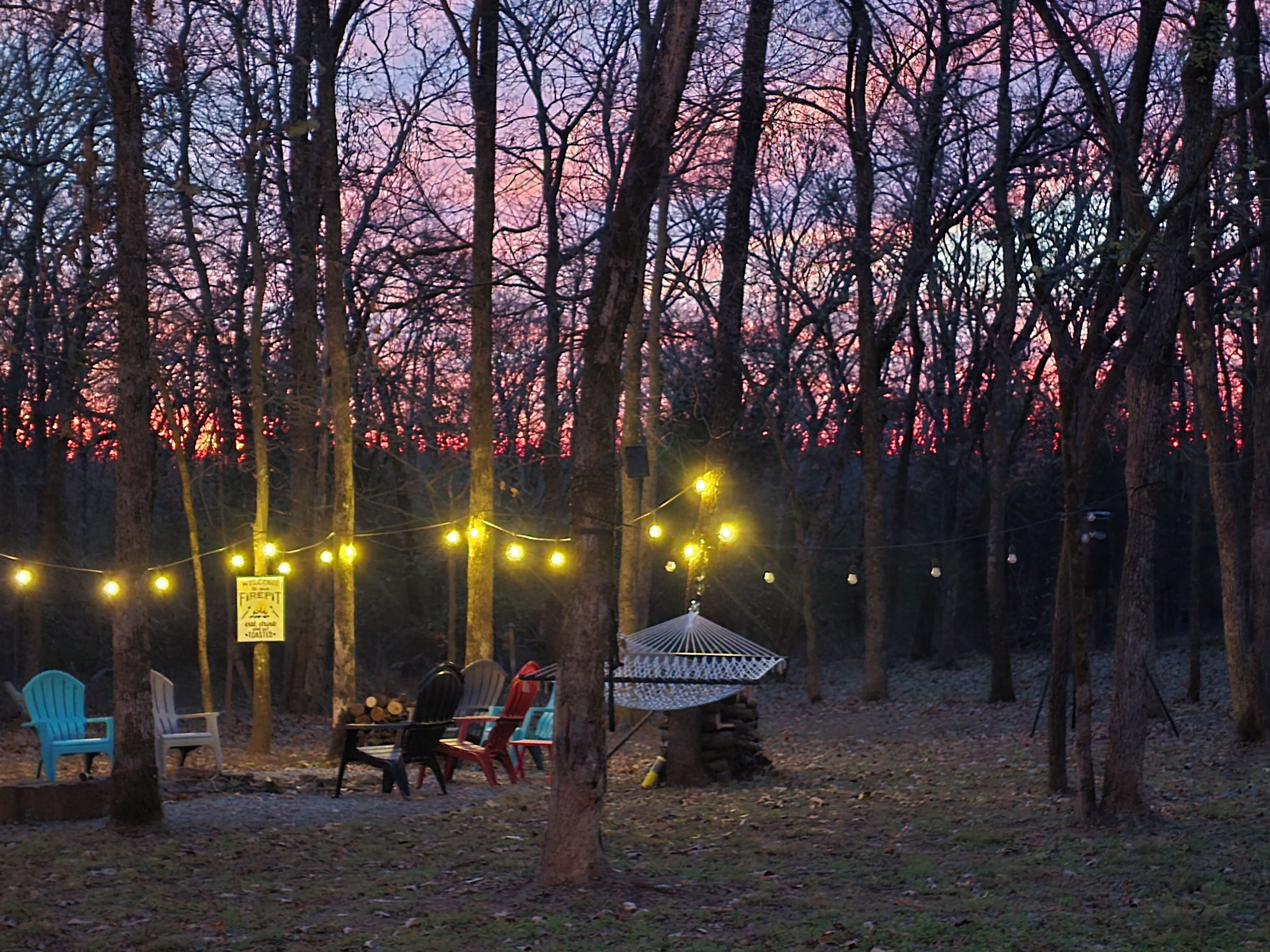 A forested area with string lights, a gazebo, and outdoor seating.