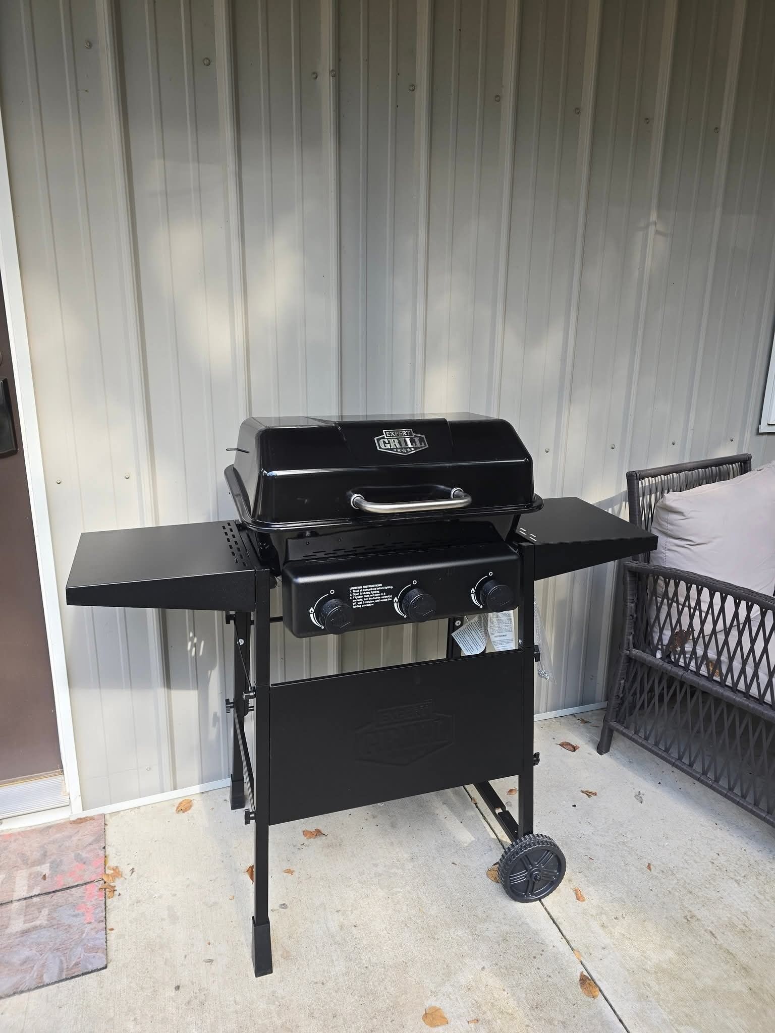 Ein schwarzer Grill mit Beistelltisch, platziert auf einer Beton-Terrasse vor einer wellenförmigen Metallwand.