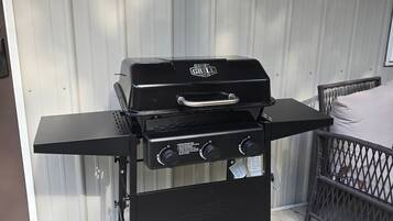 Ein schwarzer Grill mit Beistelltisch, platziert auf einer Beton-Terrasse vor einer wellenförmigen Metallwand.