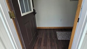 Una puerta que da a una habitación con suelo de madera, un felpudo y cuadros en la pared.