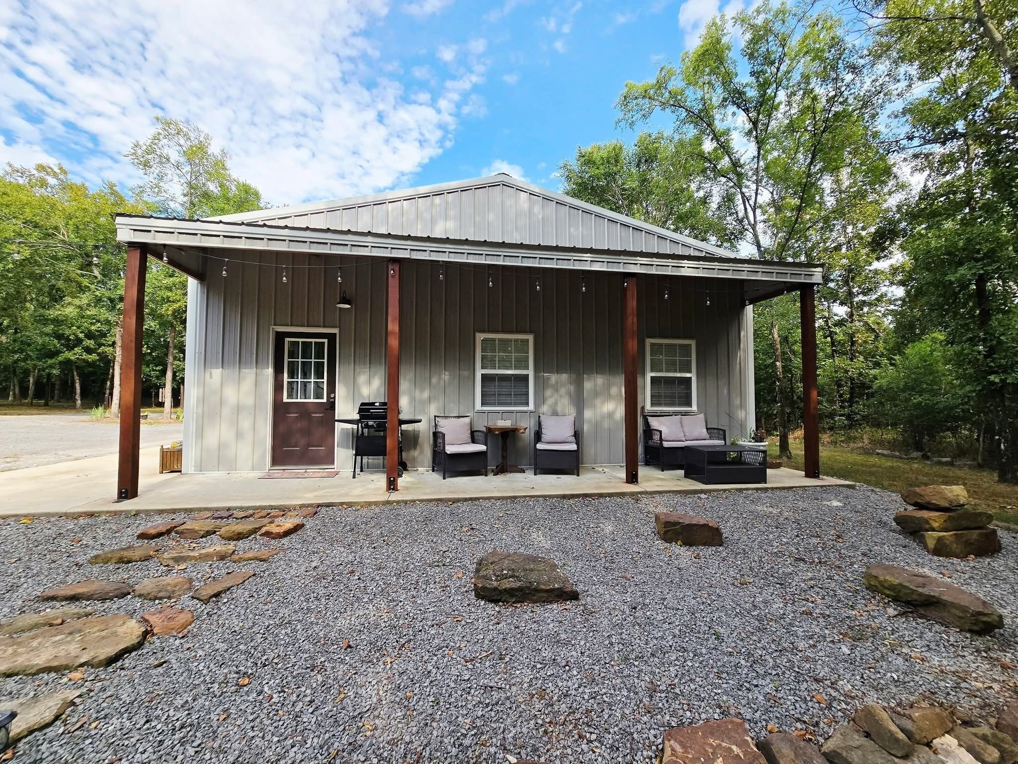A rustic metal building with a porch, outdoor seating, and a gravel driveway.