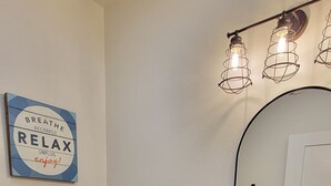Un baño con inodoro blanco, muebles de color azul oscuro, un lavabo con espejo y una lámpara de pared.