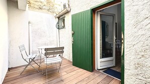 A wooden deck with a table and chairs, a green door, and a white wall with a textured surface. - Le Studio des Tilleuls, Air-Conditioned & Real Bed (Nîmes)