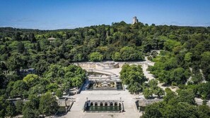 An aerial view of a park with a central fountain, pathways, and a statue on a hill.
