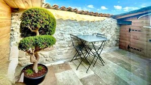 A stone wall, a potted bonsai tree, and a metal table with chairs in a courtyard. - La Tropézienne, charm and comfort in the Gard. (Saint-Geniès-de-Malgoirès)