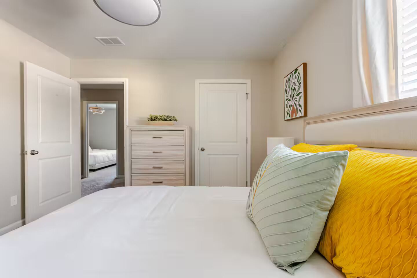 A bedroom with a bed, a dresser, and a door leading to another room.