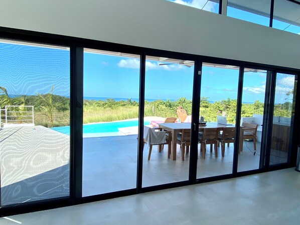 Un interior moderno con puertas de cristal grandes que dan a un área de piscina exterior, una mesa de comedor y sillas.