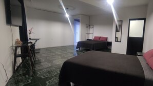 Une chambre d’hôtel avec un lit, un bureau et une chaise. Il y a un miroir sur le mur et une porte qui donne sur une autre pièce.