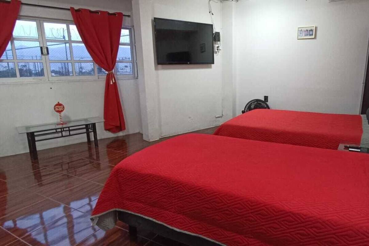 Una habitación con dos camas, televisión, banco y ventana con cortinas.