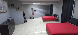 A room with two beds, a desk, a chair, a fan, and a small table. - LA PATRONA HOSTAL (Oaxaca)