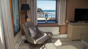 A modern living room with a view of the ocean, a comfortable chair, a television, and a radiator. - Graftons, Little Haven (Little Haven)