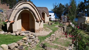 A rustic stone house with a wooden door and a thatched roof, surrounded by a stone pathway and greenery.
